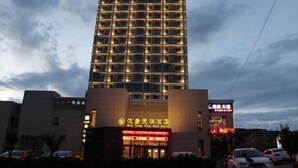 Un edificio de hotel de varios pisos con señalización iluminada, una entrada destacada y un estacionamiento al frente.