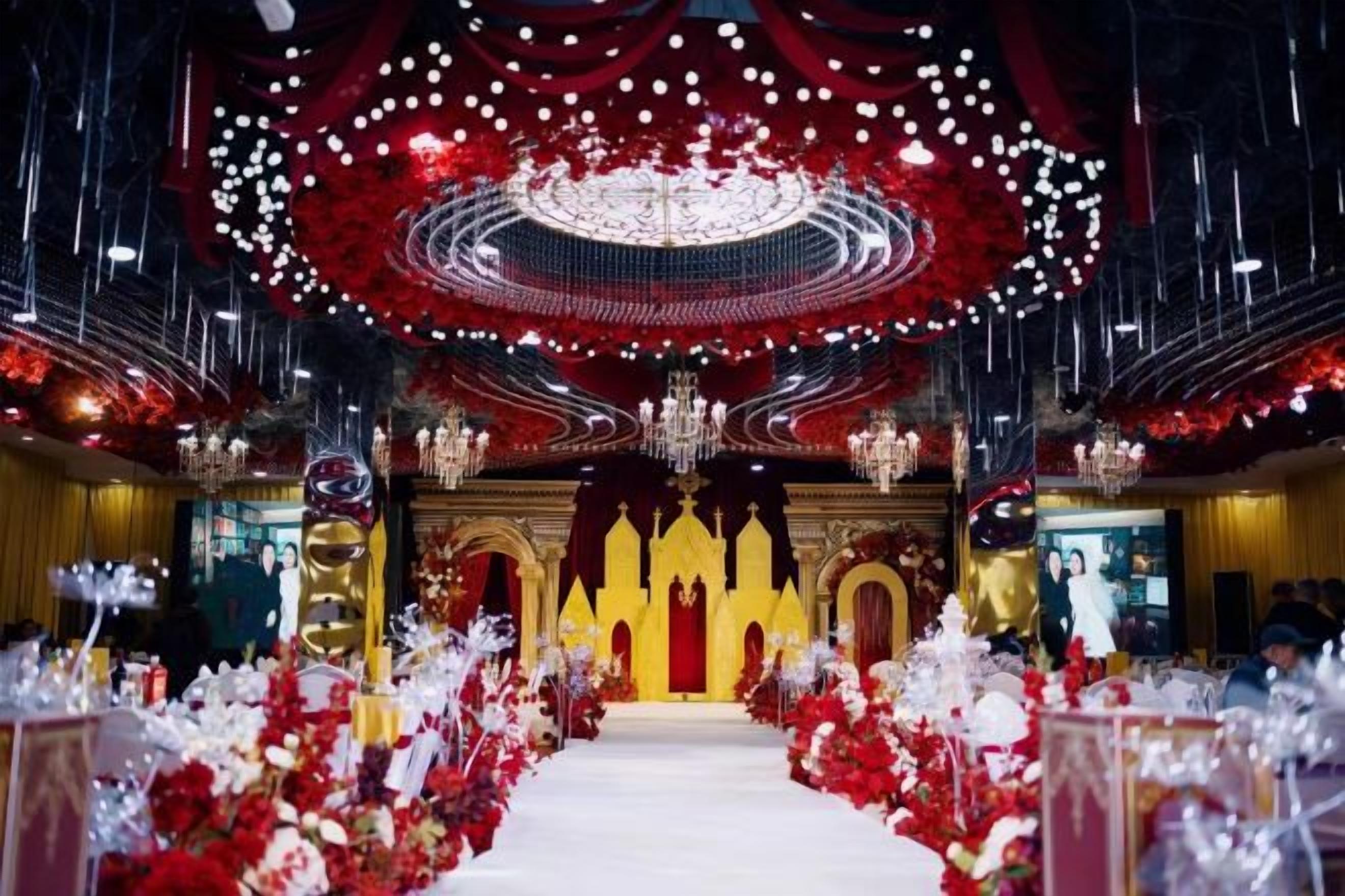 Un espacio interior con un pasillo central, arreglos florales rojos y blancos, y una araña de cristal.