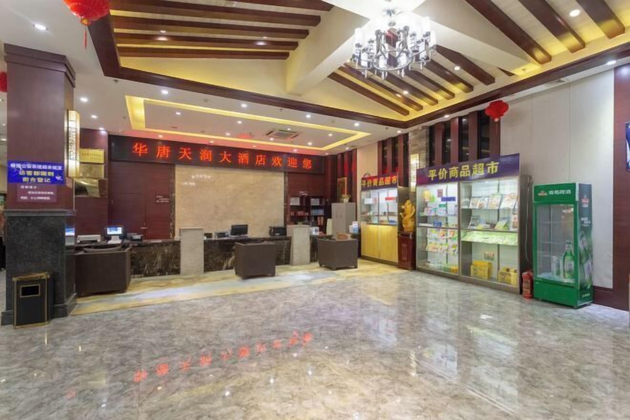 Vestíbulo de hotel con mostrador de recepción, candelabro y una vitrina con productos.