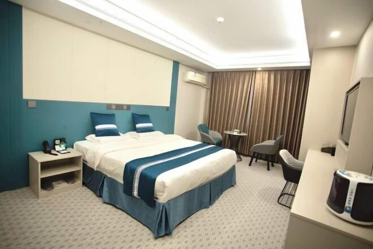 Quarto de hotel com cama, mesa de cabeceira, cadeira, escrivaninha e televisão.