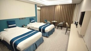Habitación de hotel con dos camas, un escritorio, una silla, un televisor y una ventana con cortinas.