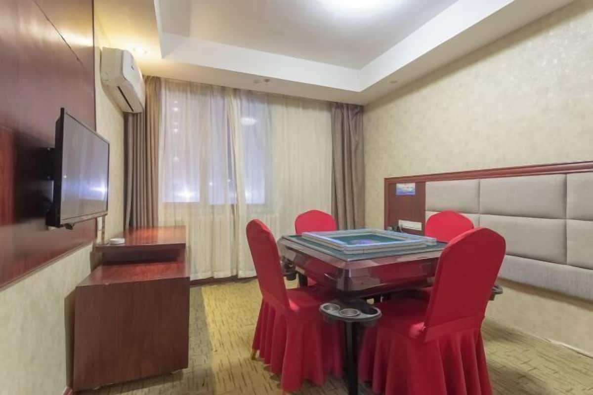 Quarto de hotel com mesa de jantar, cadeiras vermelhas, televisão e uma janela grande com cortinas.