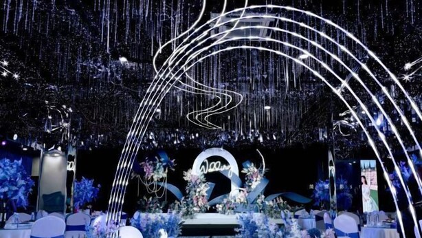 Una recepción de boda con escenario, decoración floral y un fondo que dice 'Wedding'.