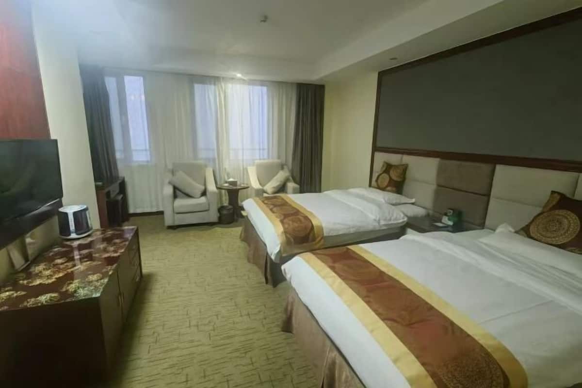 Quarto de hotel com duas camas, televisão, escrivaninha e uma cadeira.