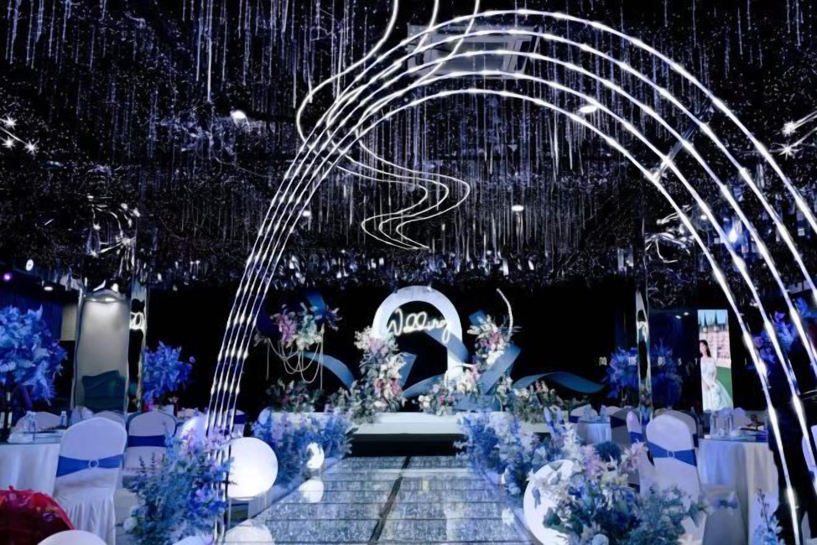 Un espacio interior para eventos con un escenario, arreglos florales y un letrero circular.