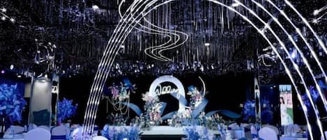 An indoor event space with a stage, floral arrangements, and a circular sign.