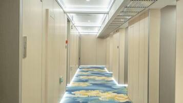 A narrow hallway with a patterned carpet, doors on both sides, and a ceiling with recessed lighting.