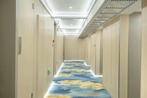 Un pasillo estrecho con alfombra estampada, puertas a ambos lados y un techo con iluminación empotrada.