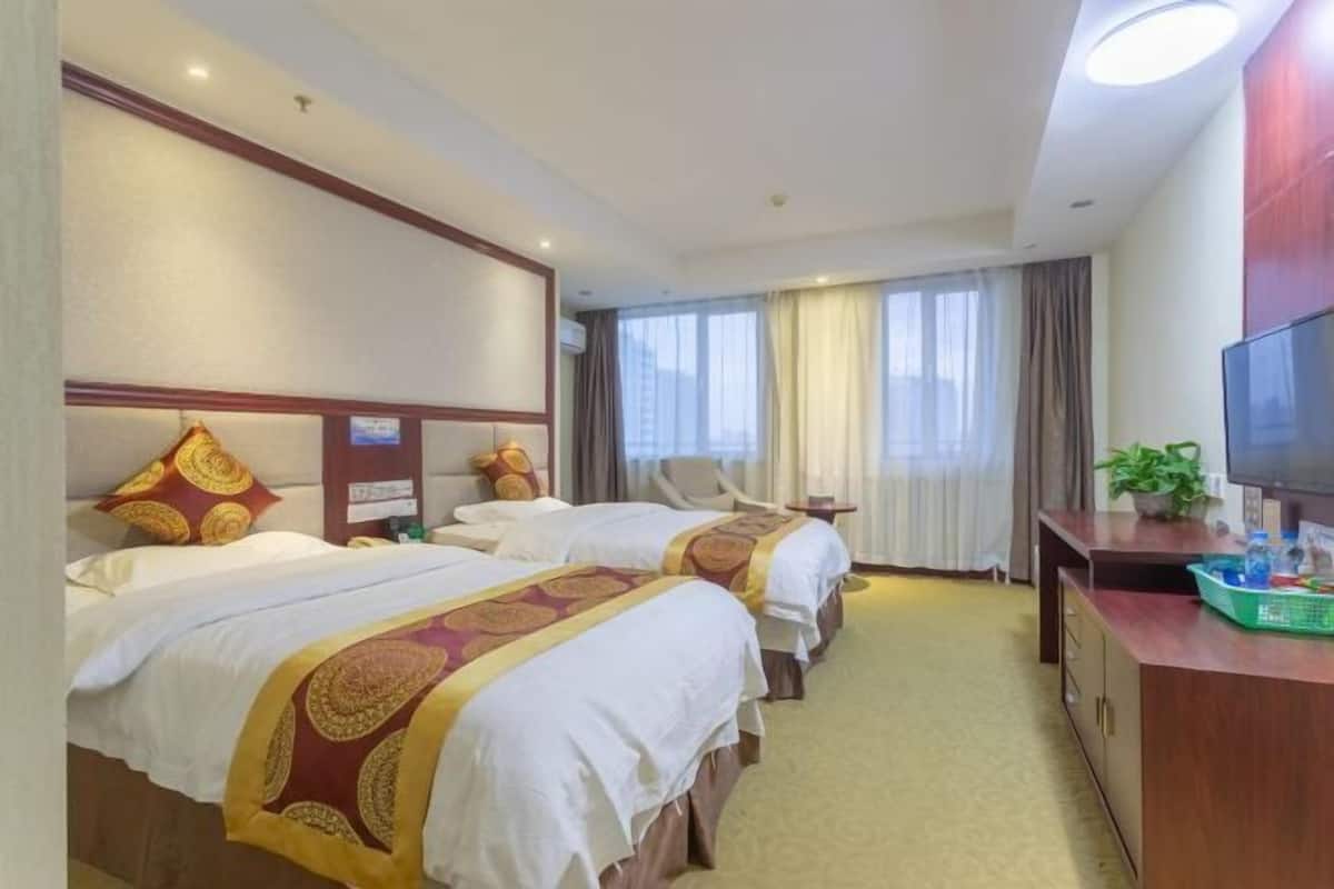 Quarto de hotel com duas camas, uma escrivaninha, televisão e uma janela com cortinas.