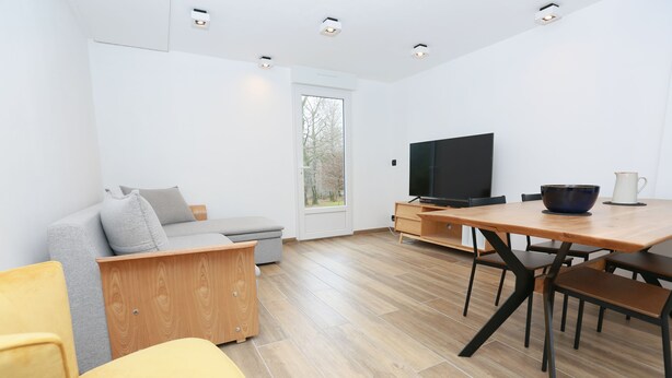En moderne stue med sofa, lænestol i gult, sofabord i træ, fjernsyn og spisebord med stole.