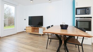 Et moderne køkken med et træspisebord, sorte stole, et fladskærms-tv og indbyggede hårde hvidevarer.