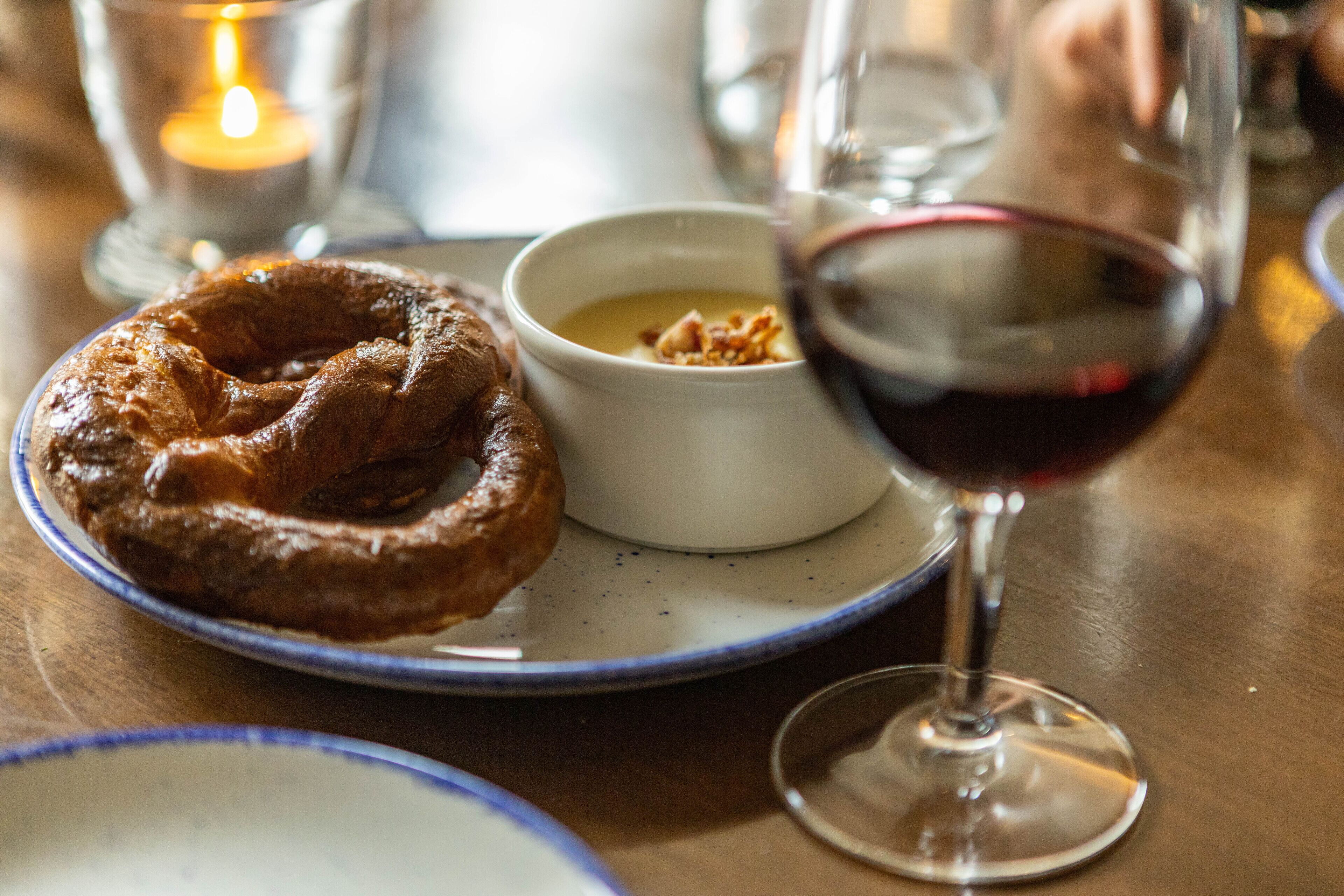A plate with a pastry, a small bowl of soup, and a glass of red wine on a table.