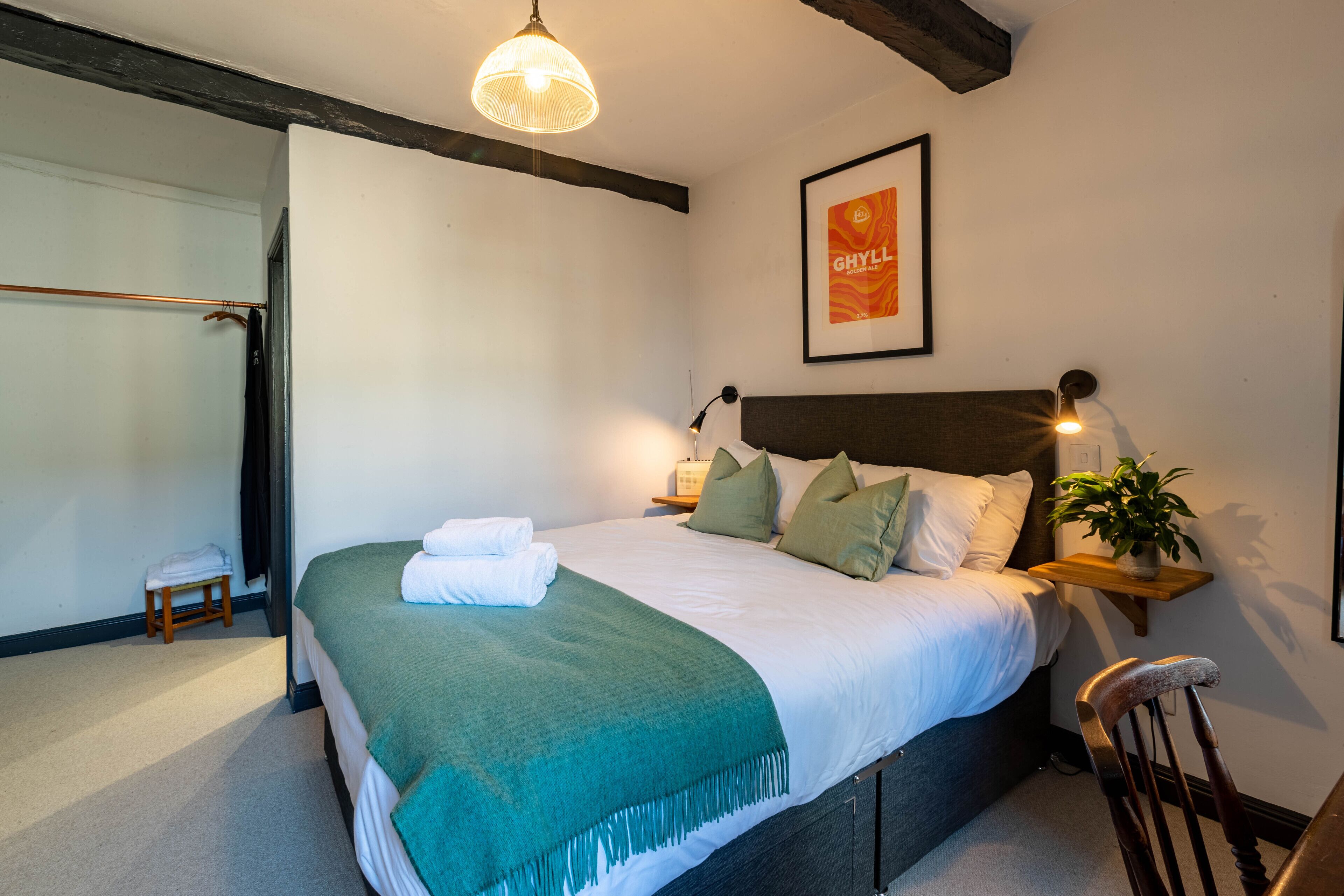 A neatly made bed with a green throw, a bedside lamp, and a framed poster on the wall.