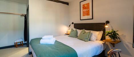 A neatly made bed with a green throw, a bedside lamp, and a framed poster on the wall.