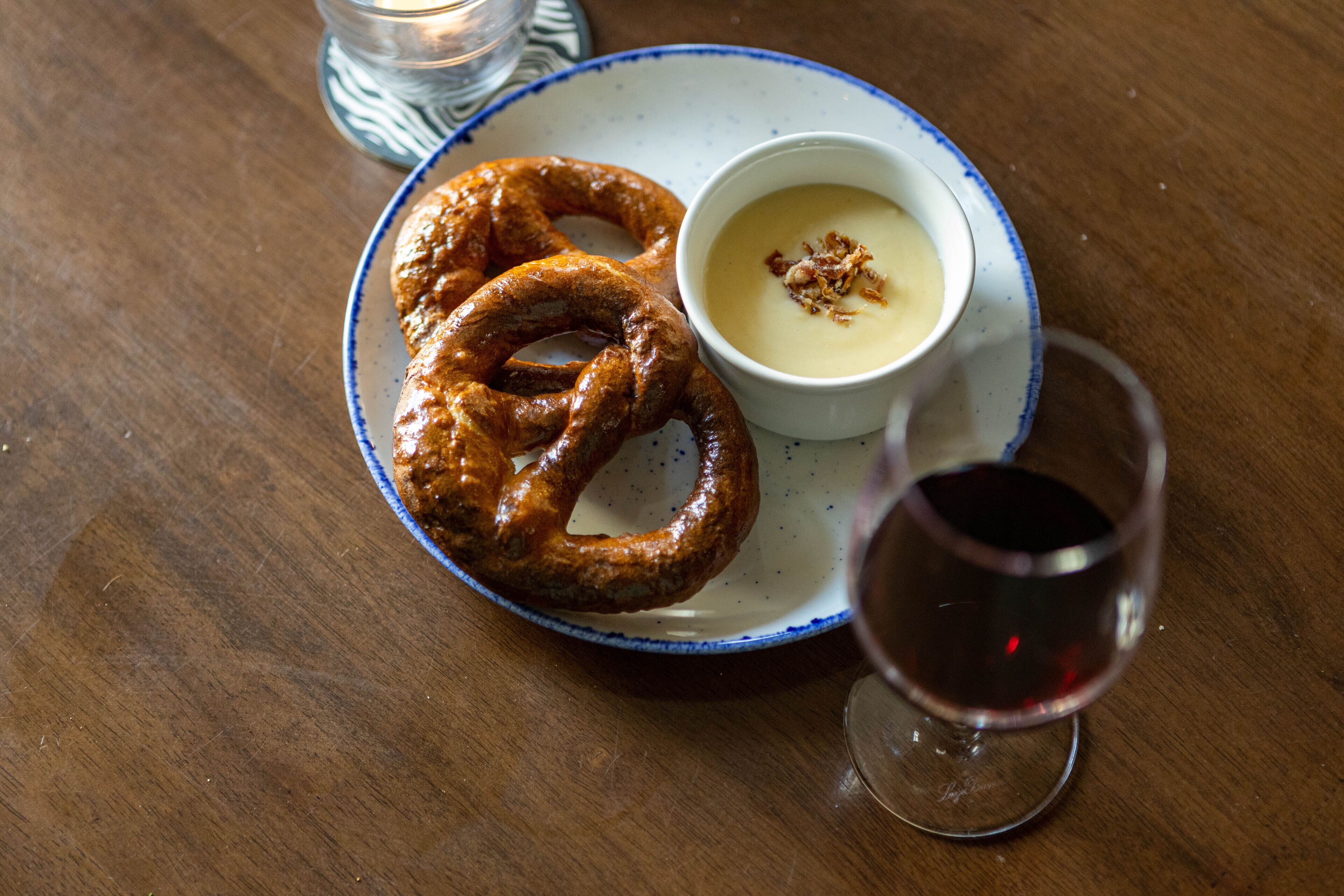 A plate with a pretzel and a bowl of soup on a table.