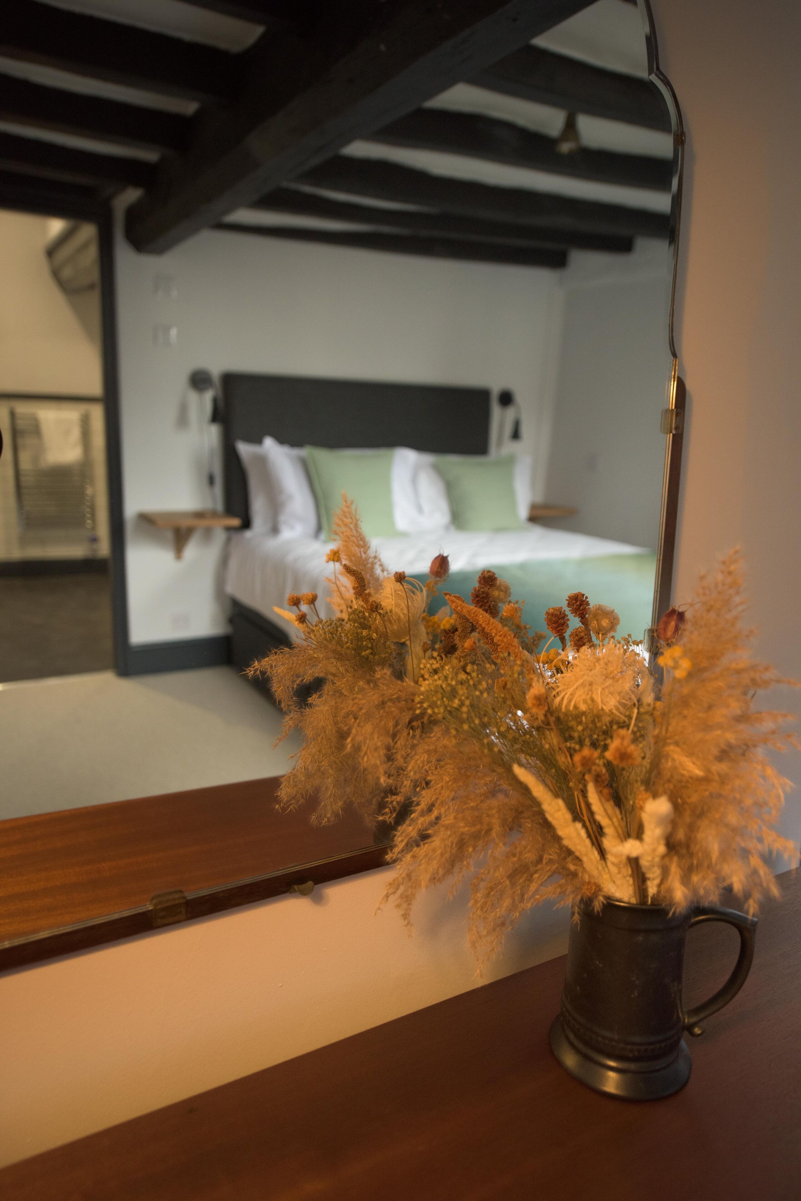 Ein Zimmer mit einem Bett, einem Nachttisch und einem Spiegel, der den Raum wiedergibt.