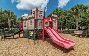 A playground with a red slide, climbing structures, and a small building with windows.