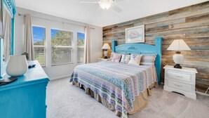 A bedroom with a wooden wall, a bed with a patterned bedspread, a ceiling fan, and a nightstand with a lamp. - End Unit Magical Retreat (Four Corners)