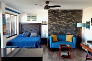 A bedroom with two beds, a sofa, a small table, a ceiling fan, and a stone wall.