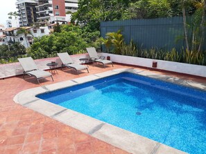 Ein Pool auf dem Dach mit vier Liegestühlen und einer gefliesten Terrasse.