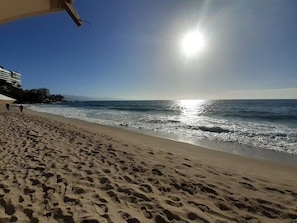 Ein Strand mit Fußabdrücken im Sand, ein klarer Himmel und das Meer im Hintergrund.