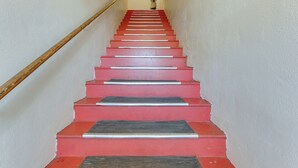 Eine Treppe mit roten Stufen und einem hölzernen Geländer, die zu einer Zwischenebene mit einem Blumentopf führt.