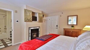Een slaapkamer met een bed, een open haard, een spiegel, een dressoir en een deur.