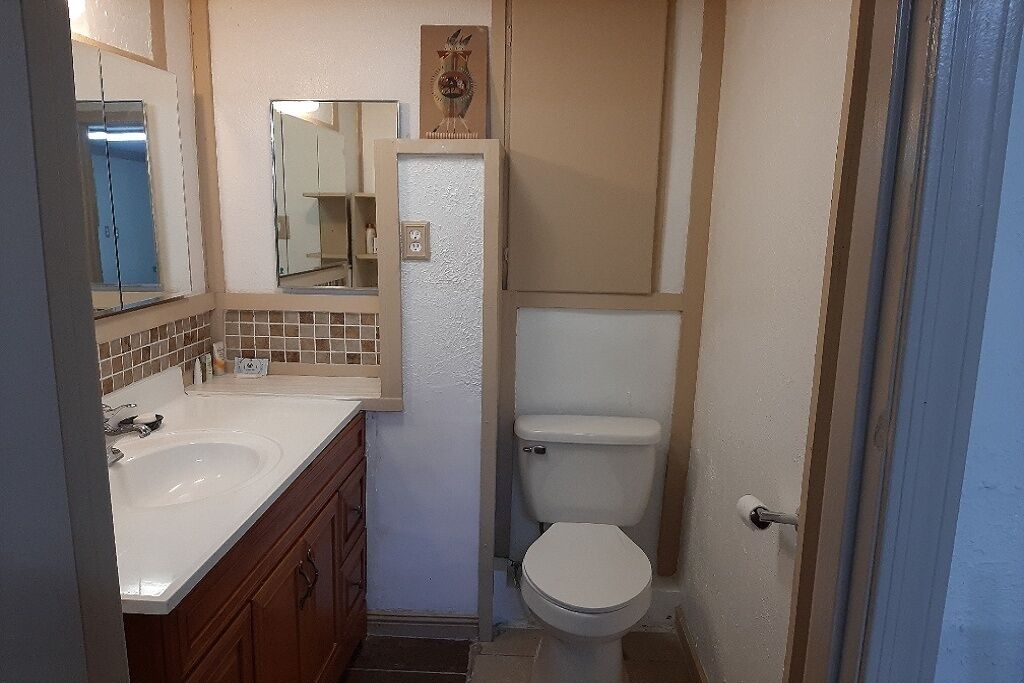 Un baño con lavamanos, espejo e inodoro blancos.