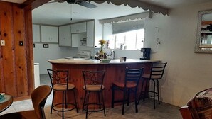 A kitchen with a central island, bar stools, and a dining table with chairs.