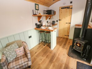 A cozy kitchen with a wooden counter, bar stools, a stove, and a plaid sofa with cushions. - The Honeybee (Pembroke)