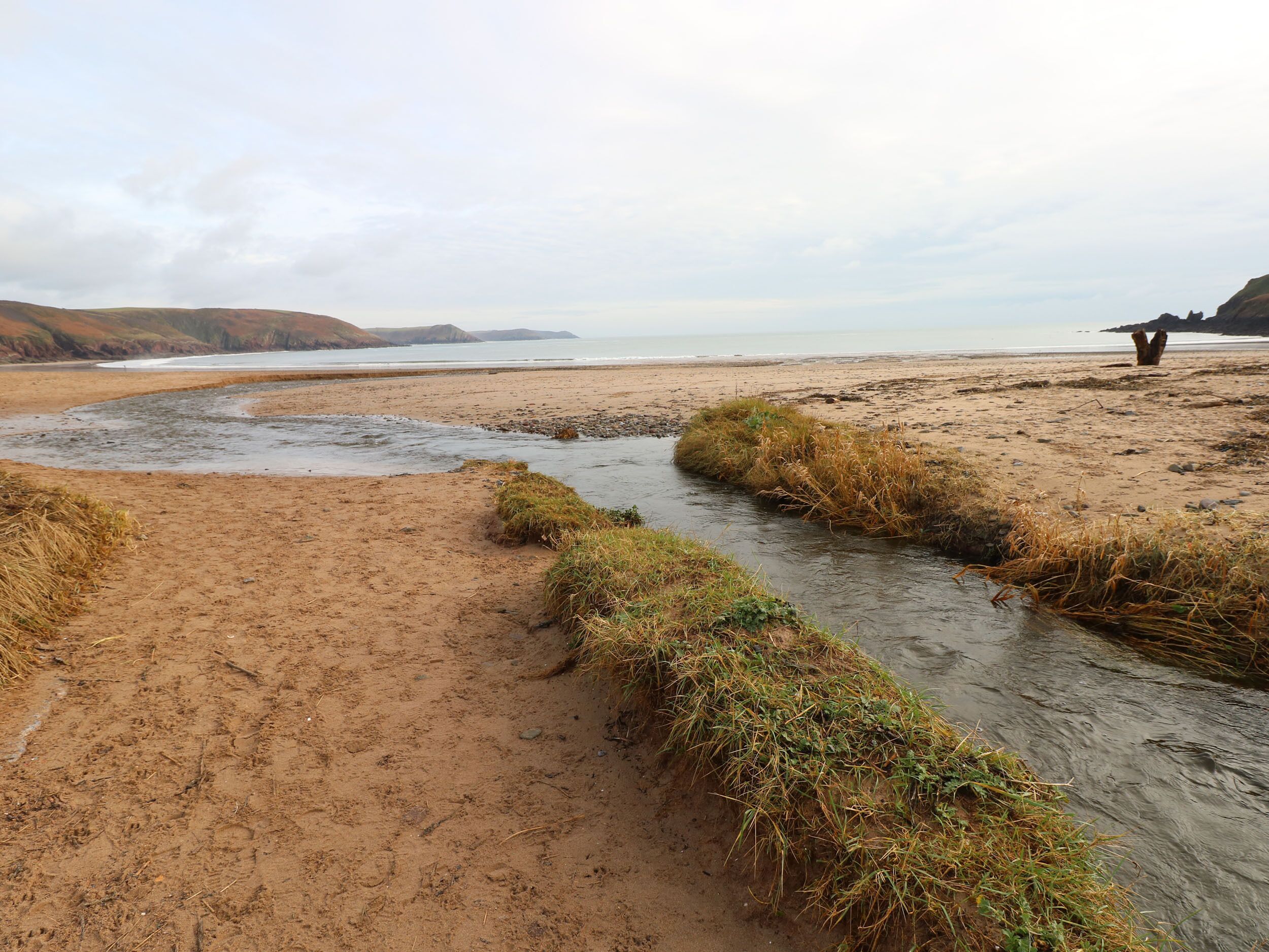 A sandy beach with a narrow water channel and grassy areas.