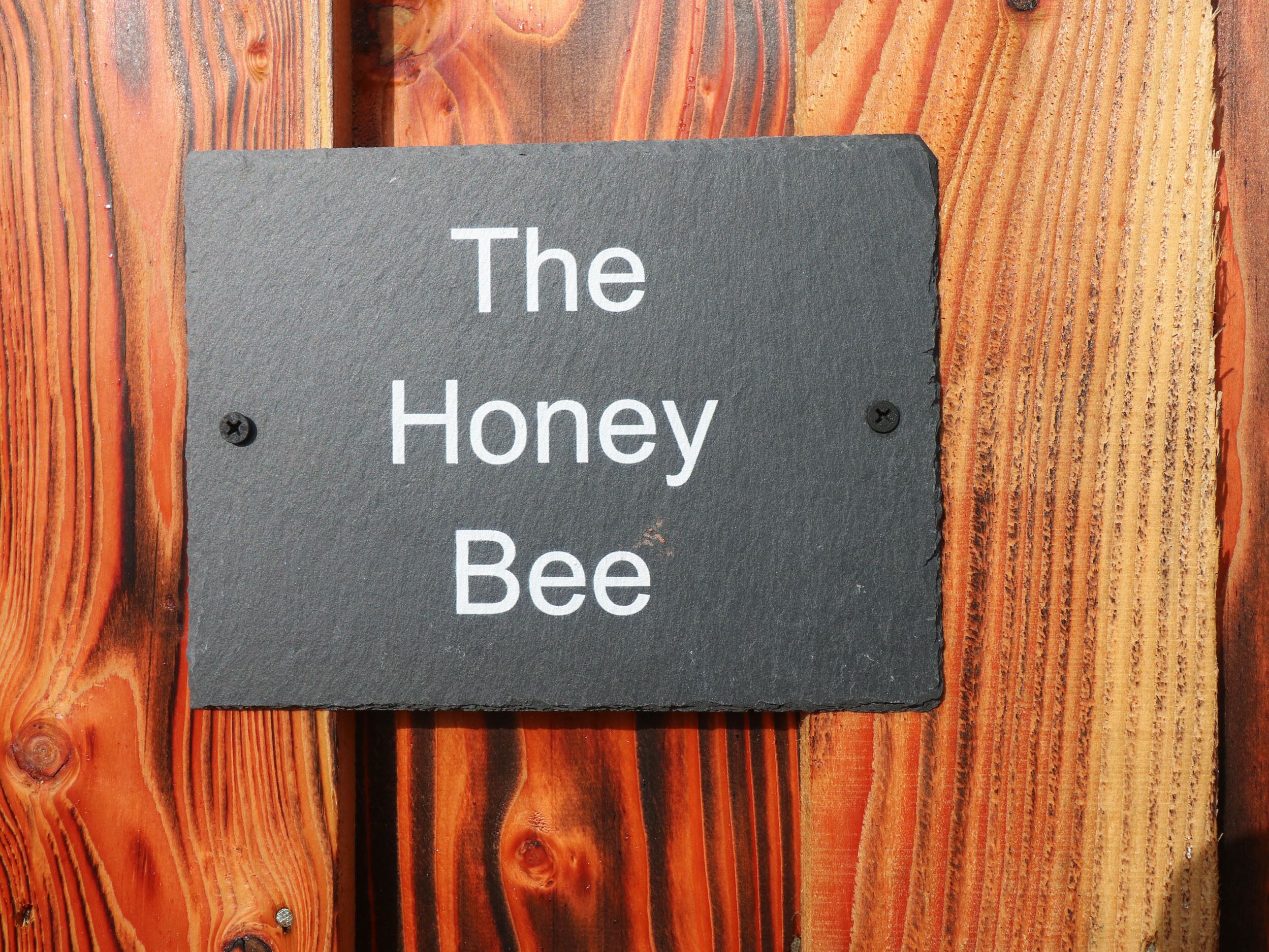 Un letrero con el texto 'The Honey Bee' sobre un fondo de madera.