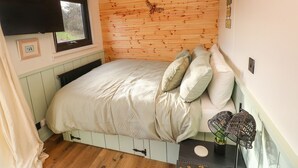 Una habitación acogedora con techo de madera, cama con colcha y almohadas blancas, ventana con vistas y televisión instalada en la pared.
