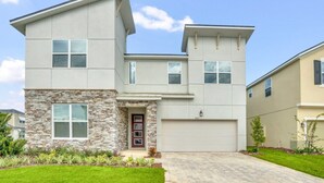 A modern two-story house with a stone facade, a garage, and a well-maintained lawn. - Exclusive Estate on Mermaid Cove 6274 (Kissimmee)