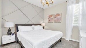 A neatly arranged bedroom with a bed, bedside tables, a chandelier, and artwork on the wall. - Exclusive Estate on Mermaid Cove 6274 (Kissimmee)