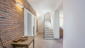 A staircase leading to a kitchen area with a brick wall and a wooden table with baskets.