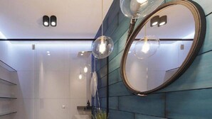 A modern bathroom with a white sink, a large mirror, and a blue tiled wall. - Green House (Poti)
