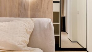 A modern bedroom with a wooden headboard, a bedside table, a bed with a white comforter, and a closet with a mirror. - Green House (Poti)