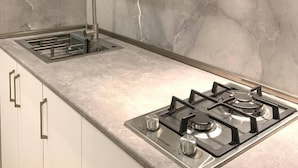 A modern kitchen with a built-in gas stove, stainless steel sink, and a white backsplash. - Green House (Poti)