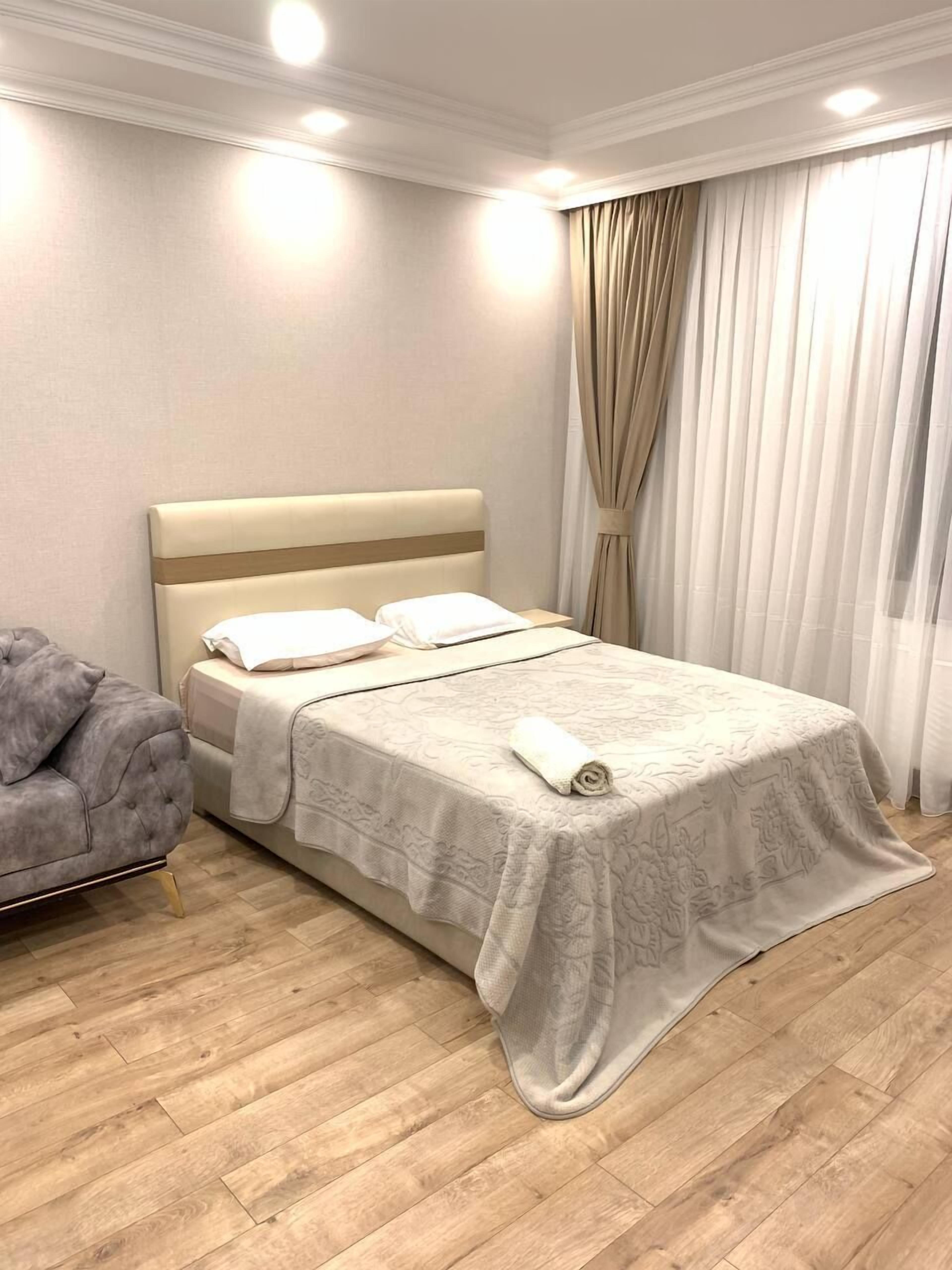 Une chambre à coucher bien rangée, avec un lit, un fauteuil gris et un plancher en bois.