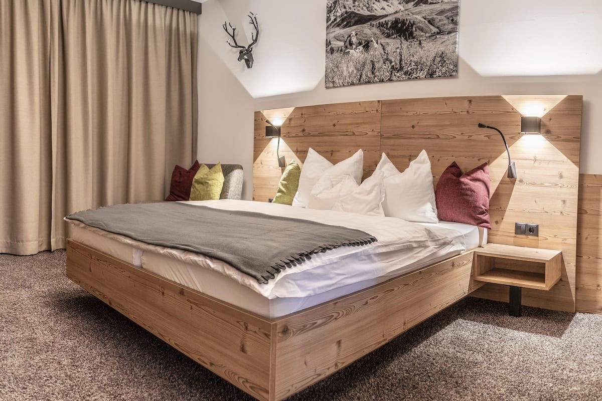 Ein modernes Schlafzimmer mit einem hölzernen Bett, einem aufgehängten Hirschgeweih, einem Gemälde einer Berglandschaft und einem Nachttisch mit Lampe.