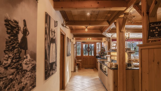 A hallway with wooden beams, tiled floor, and a Christmas tree. There are framed pictures on the walls and a sign with breakfast hours. - Sweet Cherry Boutique & Guesthouse Tyrol (Innsbruck)