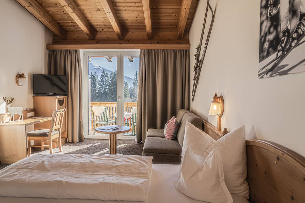 Ein Hotelzimmer mit Bett, Schreibtisch, Fernseher, Sofa und einem Balkon mit Bergblick.