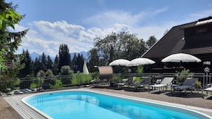 A swimming pool with lounge chairs and umbrellas, surrounded by a fence and trees. - Sweet Cherry Boutique & Guesthouse Tyrol (Innsbruck)
