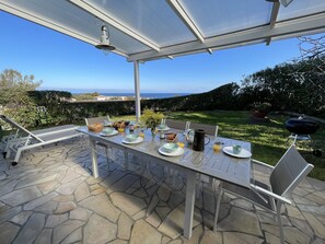 Une terrasse extérieure avec une table dressée pour le petit-déjeuner, donnant sur un jardin et la mer.
