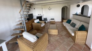 Een ruime woonkamer met een hoge plafond, een open haard en een trap naar een hoger niveau.