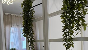 Una habitación moderna con literas, una planta colgante, un radiador y vistas al exterior a través de cortinas translúcidas.