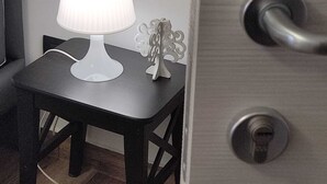 Una habitación con una pequeña mesa, una lámpara blanca y un árbol decorativo en la pared.