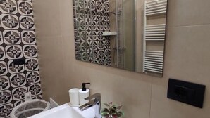 Un baño con lavamanos blanco, espejo, ducha y azulejos estampados.