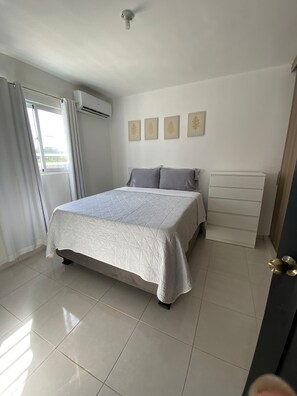 A bedroom with a bed, a dresser, and a window with curtains.